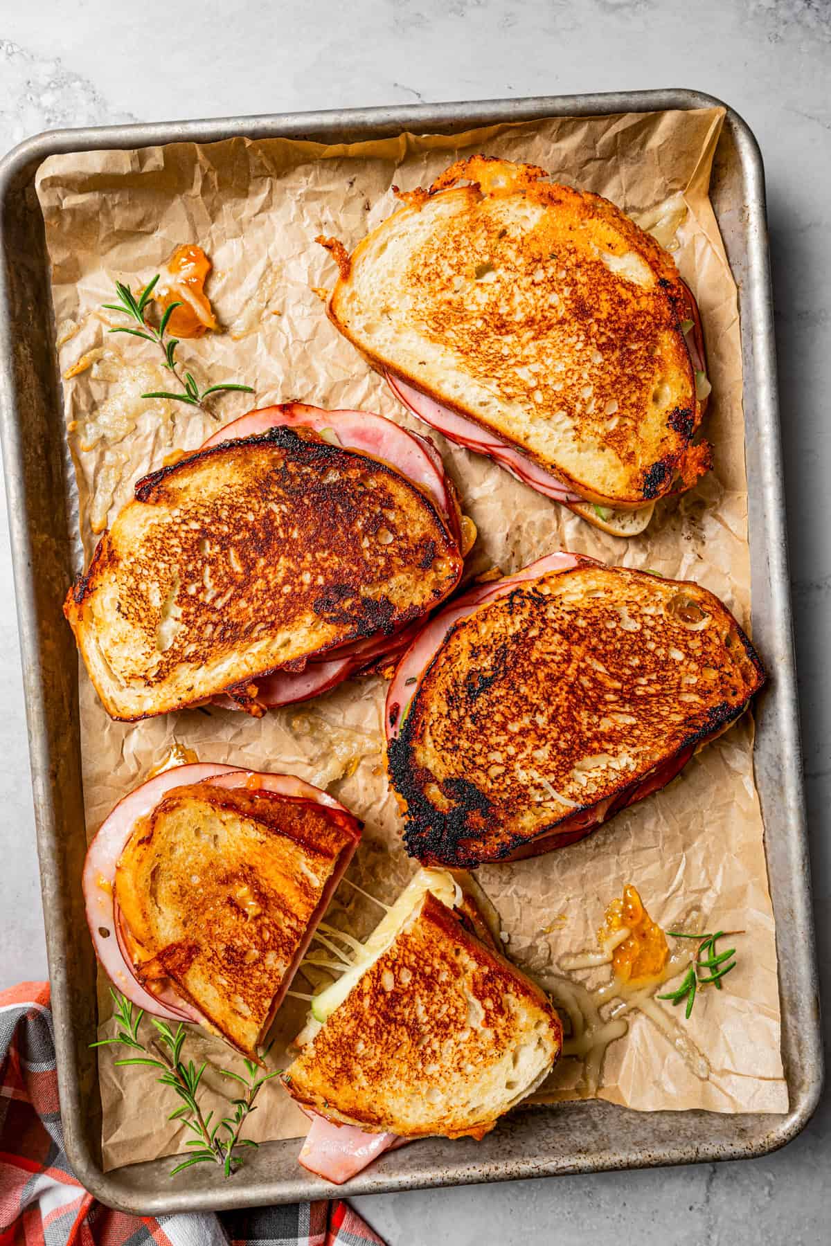 Overhead view of four apple grilled cheese sandwiches on a parchment-lined rimmed baking sheet.