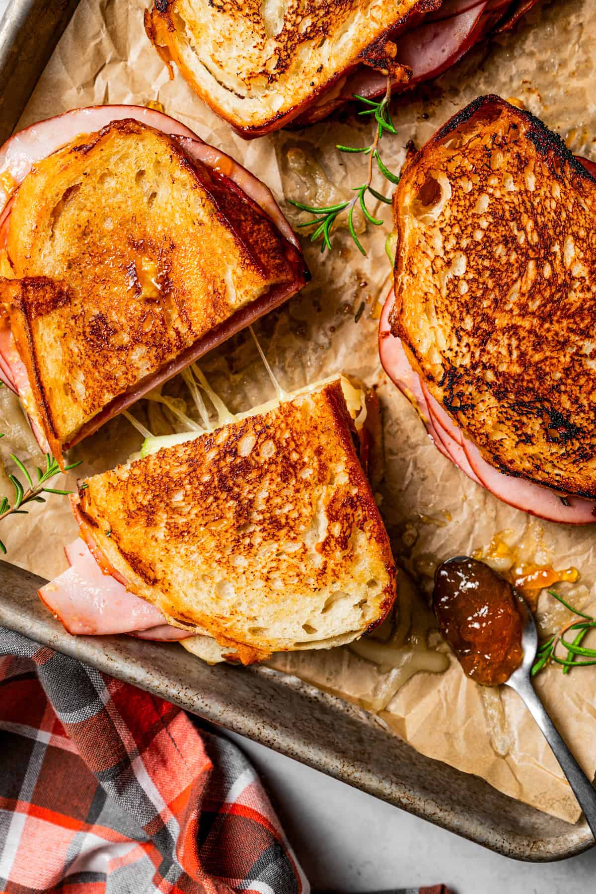 Apple grilled cheese sandwich cut in half on a parchment-lined rimmed baking sheet next to another grilled cheese.