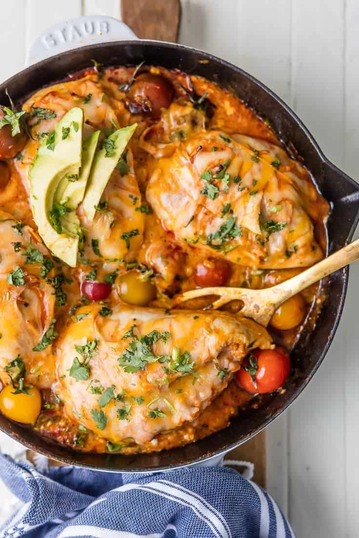 Enchilada stuffed chicken in a skilled topped with fresh herbs and avocado slices