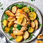 Honey garlic lemon chicken breast cut into slices, surrounded by roasted potatoes and lemon slices on a plate.