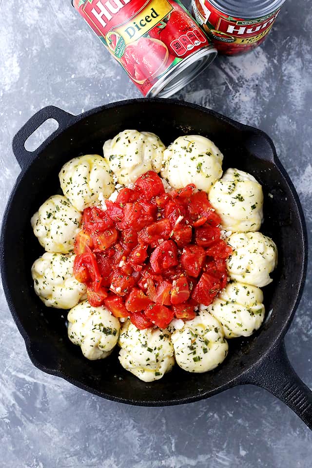 Overhead view of dough balls arranged in a ring with diced tomatoes in the middle in a cast iron skillet