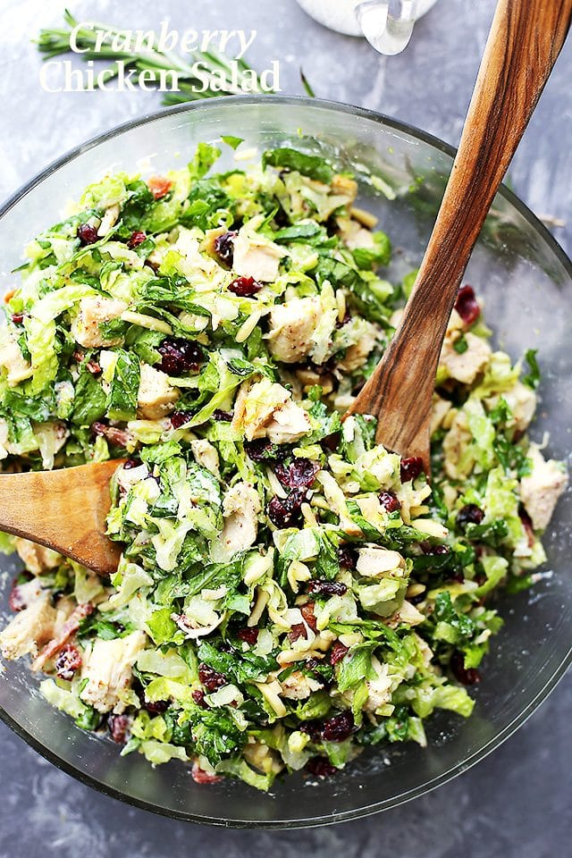 Overhead view of cranberry chicken salad in a glass bowl with two wooden salad servers.