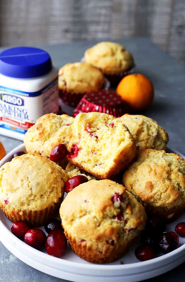 Side shot of corn muffins served on a plate with one of the muffins cut in half to show the fluffy and soft interior.