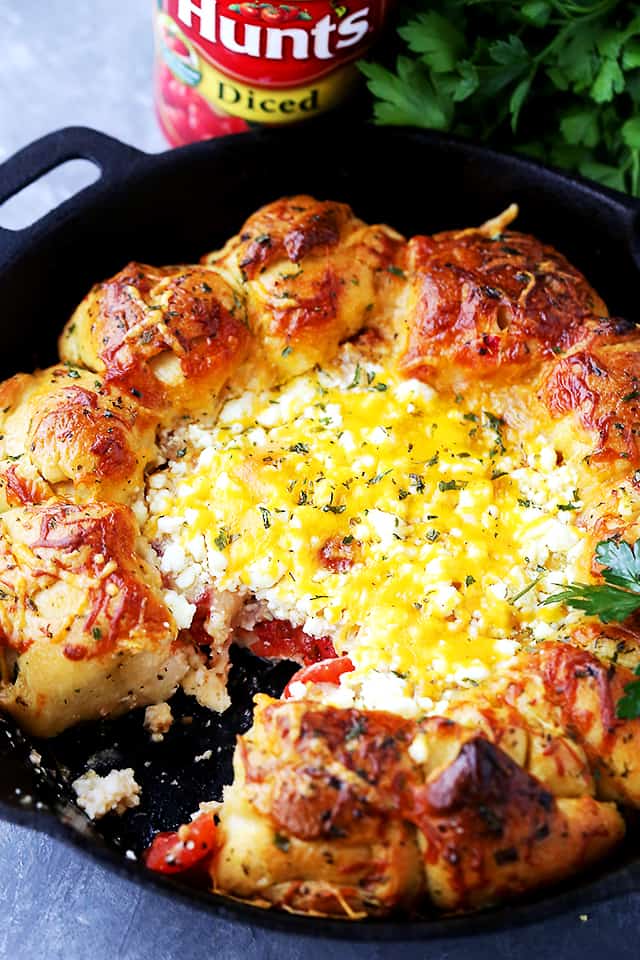 Soft and buttery pull apart rolls baked around a warm feta cheese dip in a cast-iron skillet with one roll removed. 