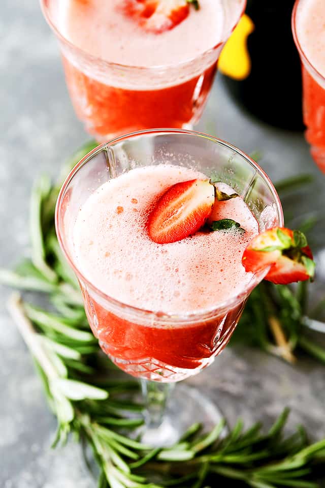 Overhead view of a Rossini cocktail garnished with fresh strawberries, with rosemary sprigs below.