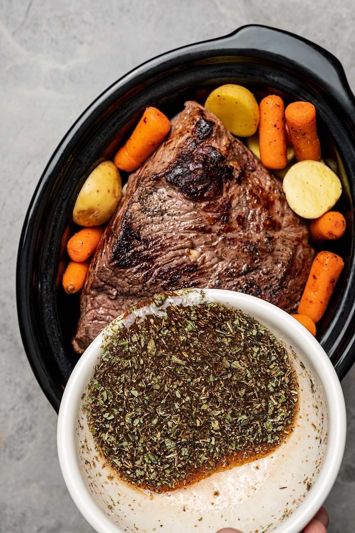 Pouring balsamic marinade over a pot roast in a slow cooker.