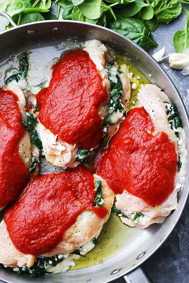 Tomato sauce spooned over raw stuffed chicken.