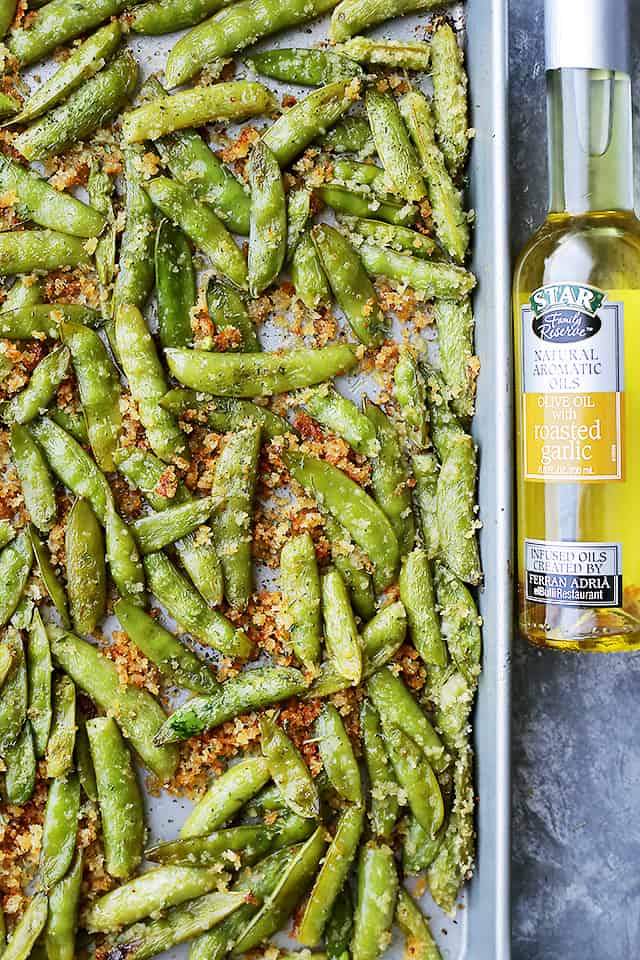 Roasted Snap Peas on a baking sheet with a bottle of olive oil set next to the baking sheet.