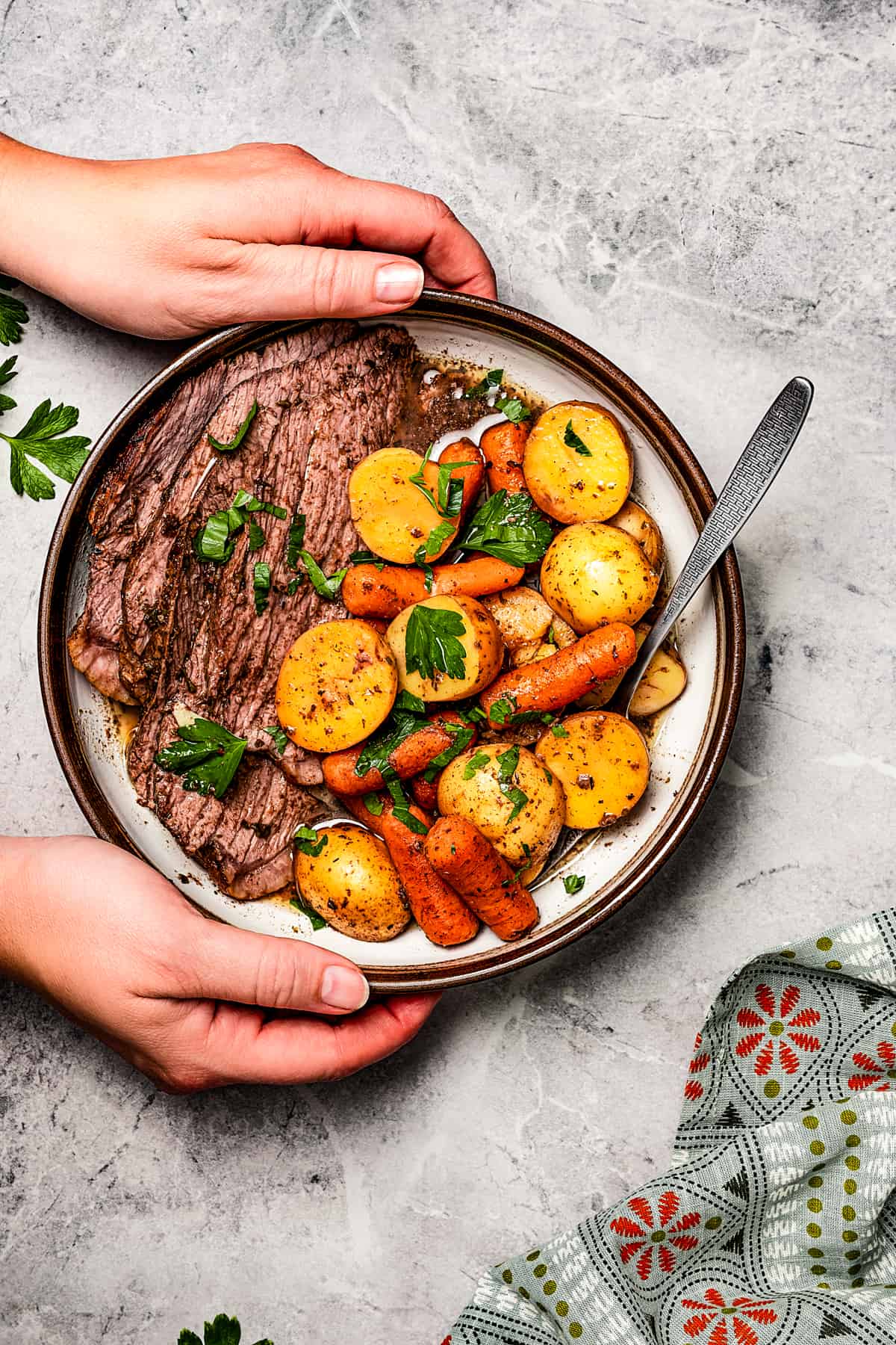 Hands picking up a dinner plate with a helping of slow cooker balsamic pot roast, potatoes, and carrots.
