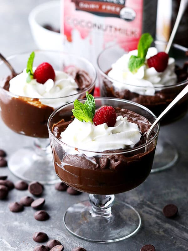 Three glasses of avocado chocolate mousse topped with whipped cream, raspberries, and mint leaves.