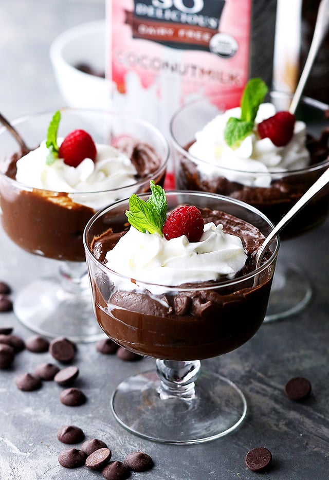 Three glasses of avocado chocolate mousse topped with whipped cream, raspberries, and mint leaves.