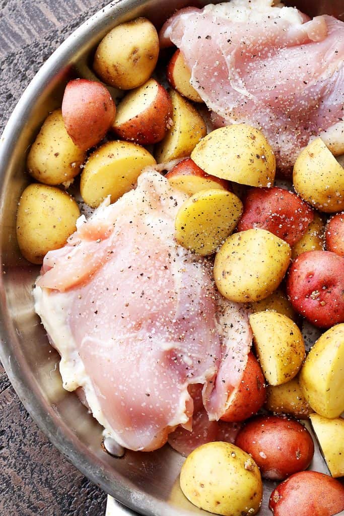 Raw chicken thighs and small potatoes in a skillet.