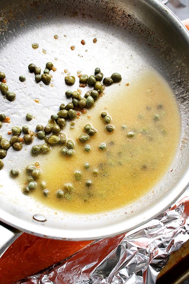 A skillet cooking piccata sauce and capers.