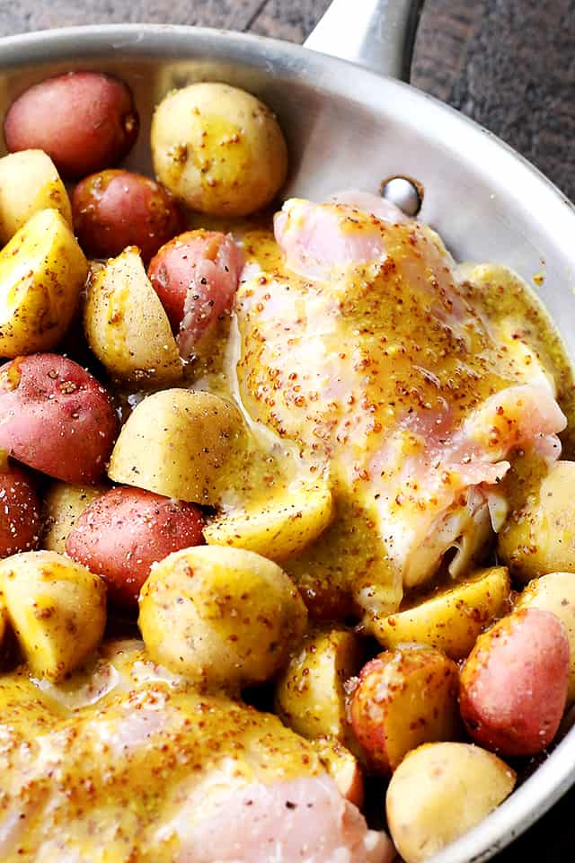 Raw chicken thighs and halved baby potatoes topped with maple syrup and mustard dressing.