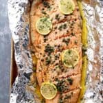A whole filet of salmon placed on foil and topped with lemon slices and garnish.