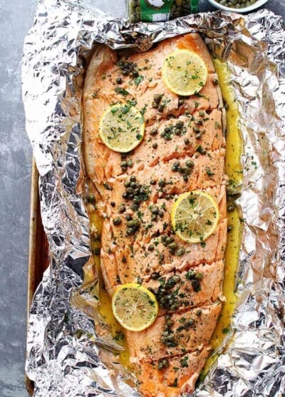 A whole filet of salmon placed on foil and topped with lemon slices and garnish.