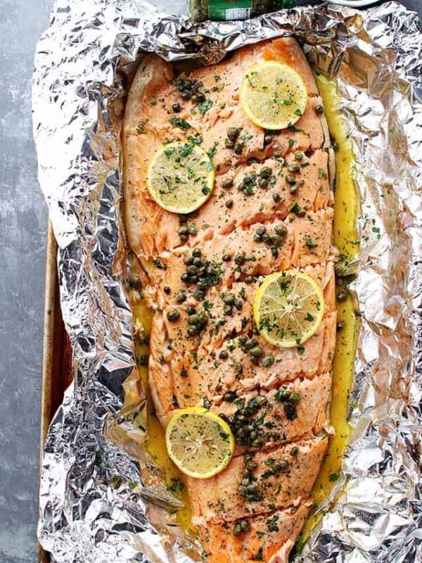 A whole filet of salmon placed on foil and topped with lemon slices and garnish.