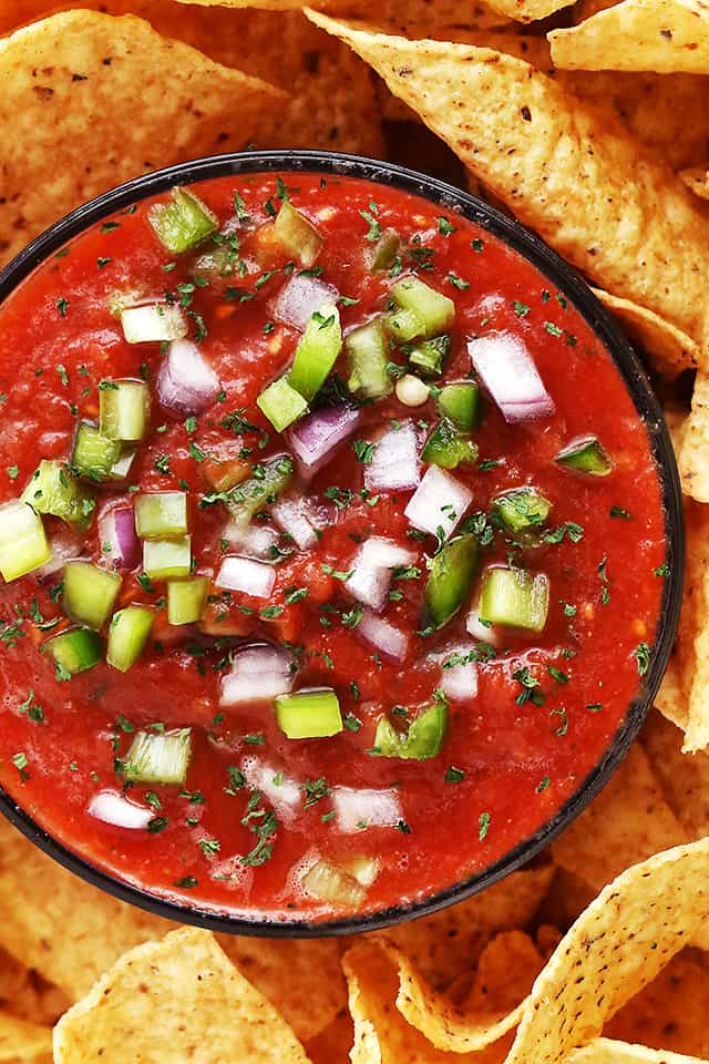 Fresh tomato salsa served in a bowl with tortilla chips arranged around it.