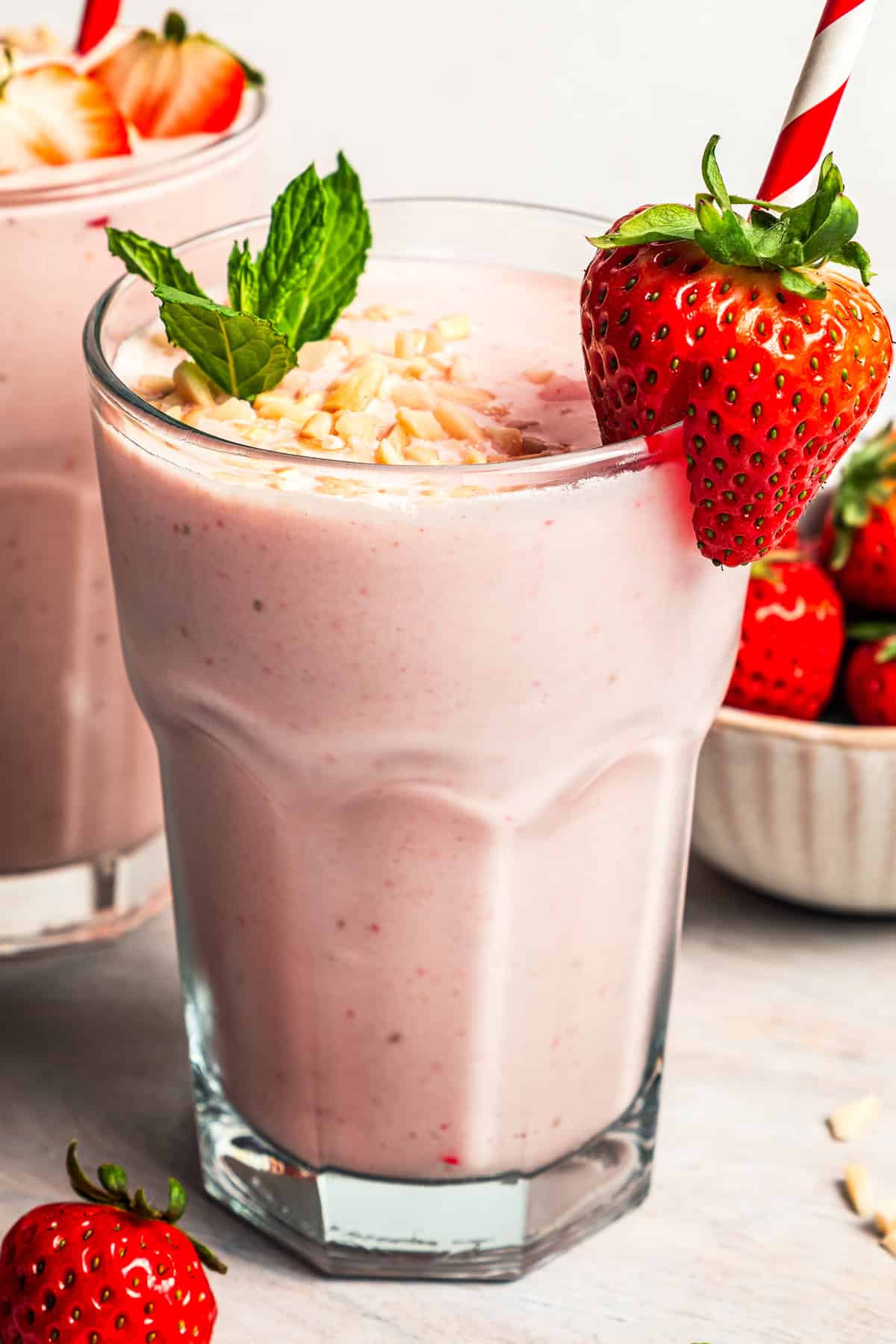 A strawberry protein shake served in a drinking glass, garnished with a strawberry on the rim and mint leaves.