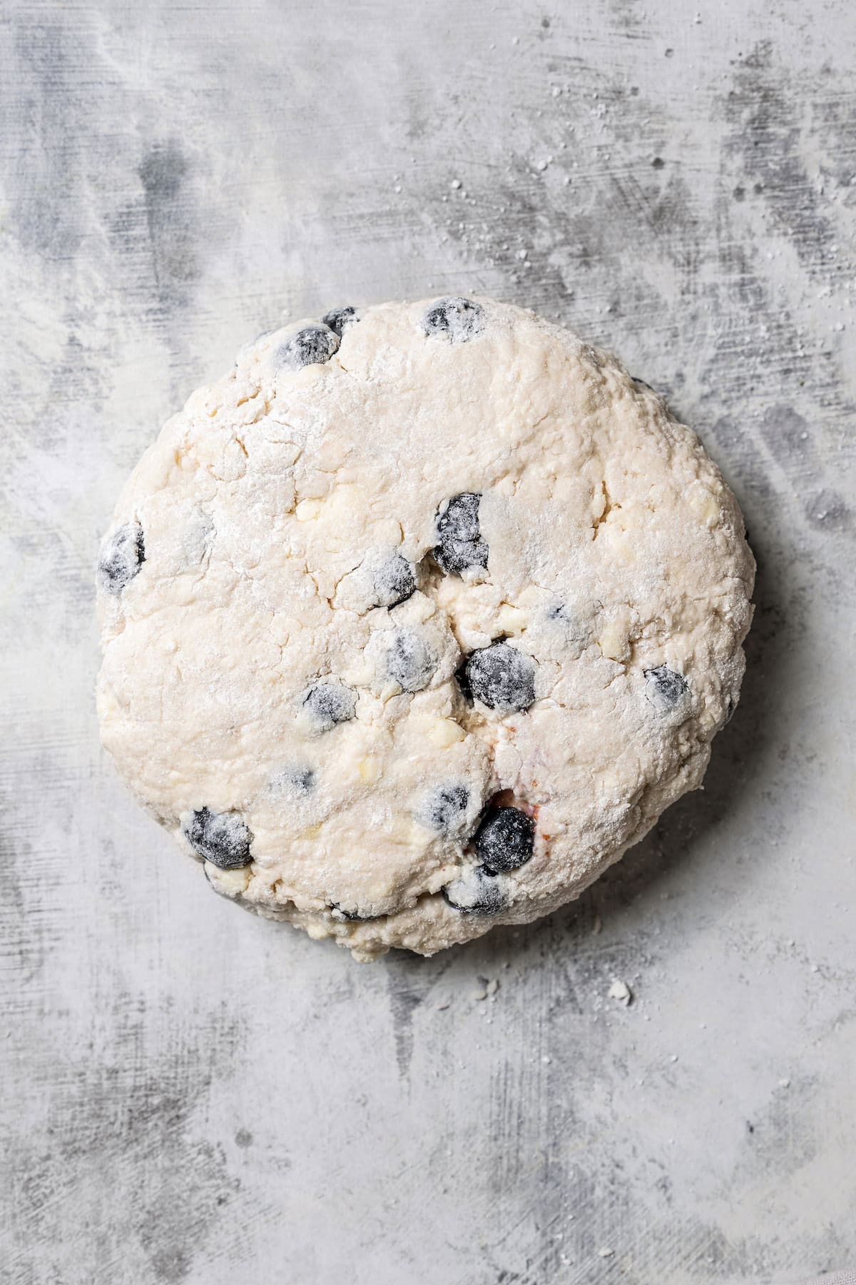 These easy blueberry biscuits are tender, buttery, and bursting with fresh blueberries! Enjoy them for breakfast, brunch, or as a snack. Blueberry biscuit dough shaped into a disc on a floured countertop.