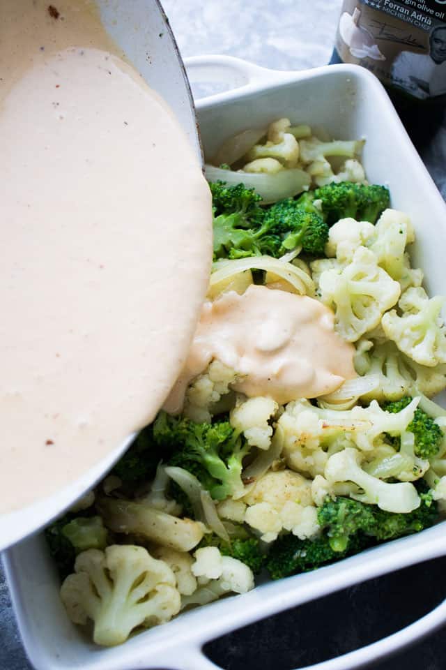 Pouring a cheese sauce over broccoli and cauliflower florets.