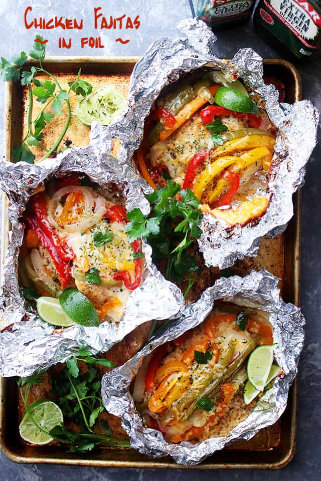 Overhead shot of a baking sheet holding three chicken fajitas in foil sheets.