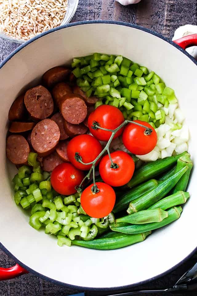 A pot filled with fresh celery, onion, okra, sausage and tomatoes