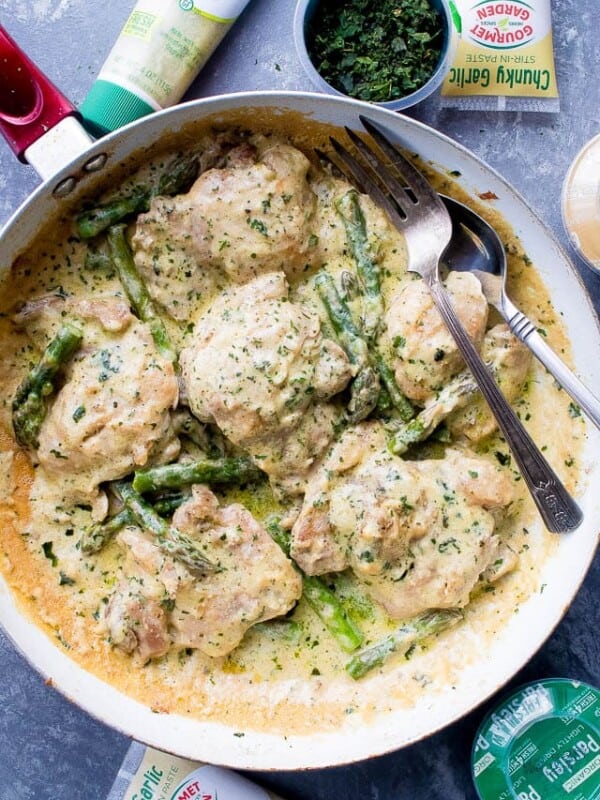 Chicken and asparagus in a skillet with a fork, surrounded by various ingredients.