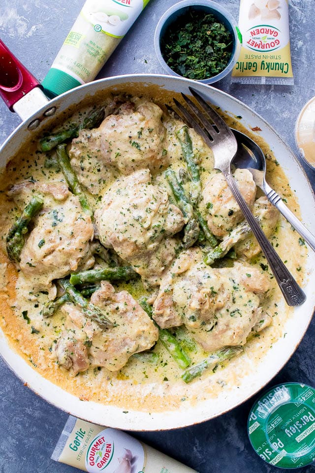 Creamy garlic chicken with asparagus in a skillet with a fork, surrounded by various ingredients.