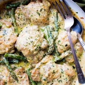 Creamy garlic chicken with asparagus in a skillet with a fork.