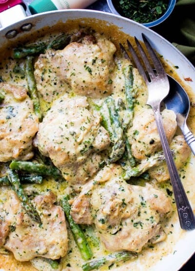 Creamy garlic chicken with asparagus in a skillet with a fork.