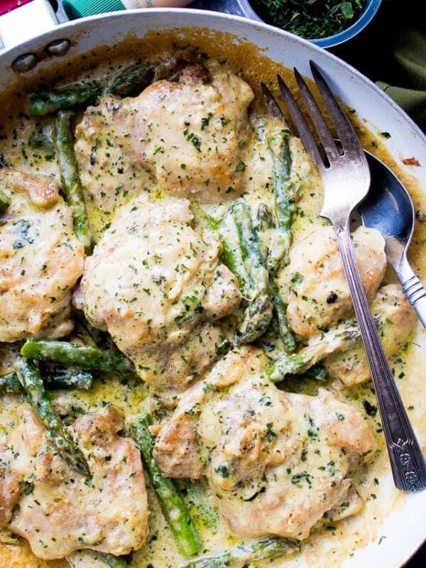 Creamy garlic chicken with asparagus in a skillet with a fork.