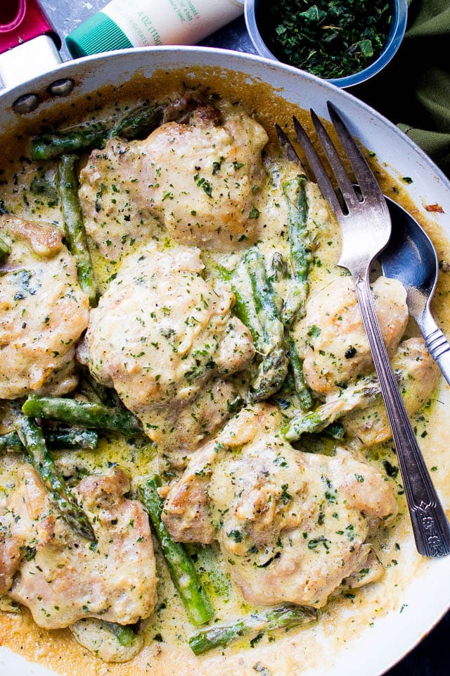 Creamy garlic chicken with asparagus in a skillet with a fork.