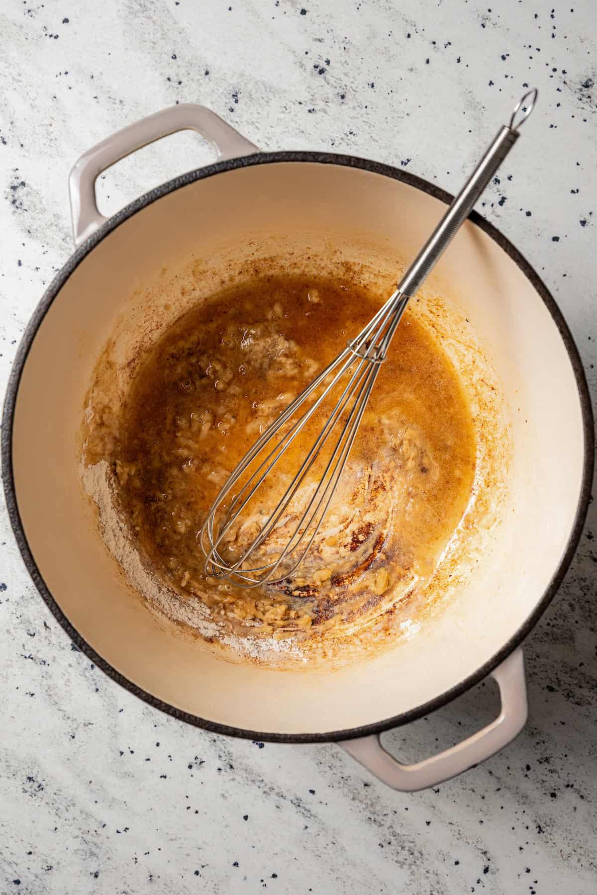 A whisk resting in a large pot with a roux of flour and butter.