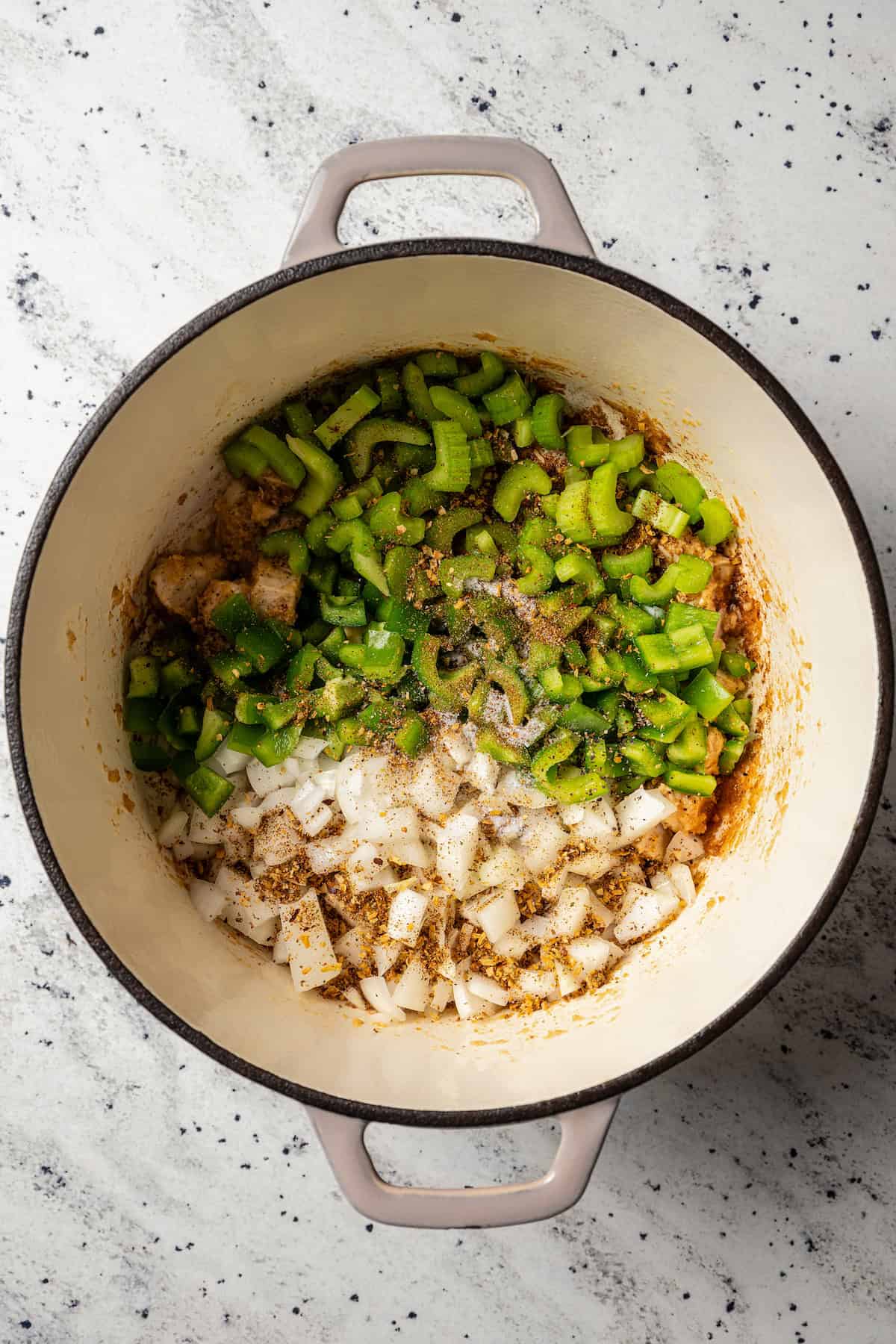 Seasonings added to sautéed veggies and chicken in a large pot.