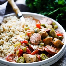A fork in a white plate filled with sausage, chicken, veggies and brown rice