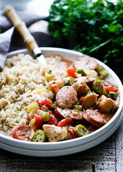 A fork in a white plate filled with sausage, chicken, veggies and brown rice