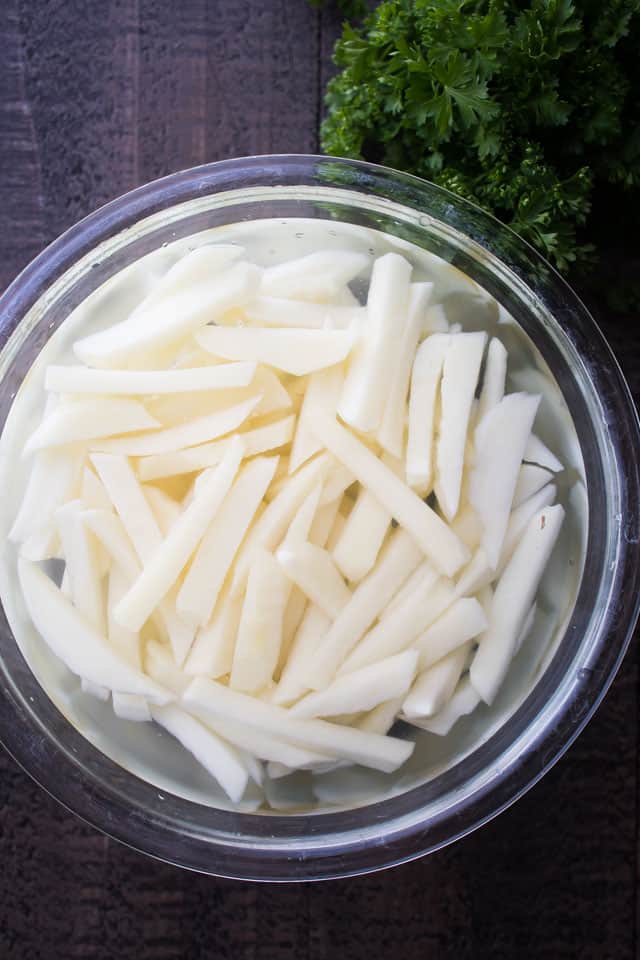 Potatoes cut into fries and soaking in a mixing bowl with water.