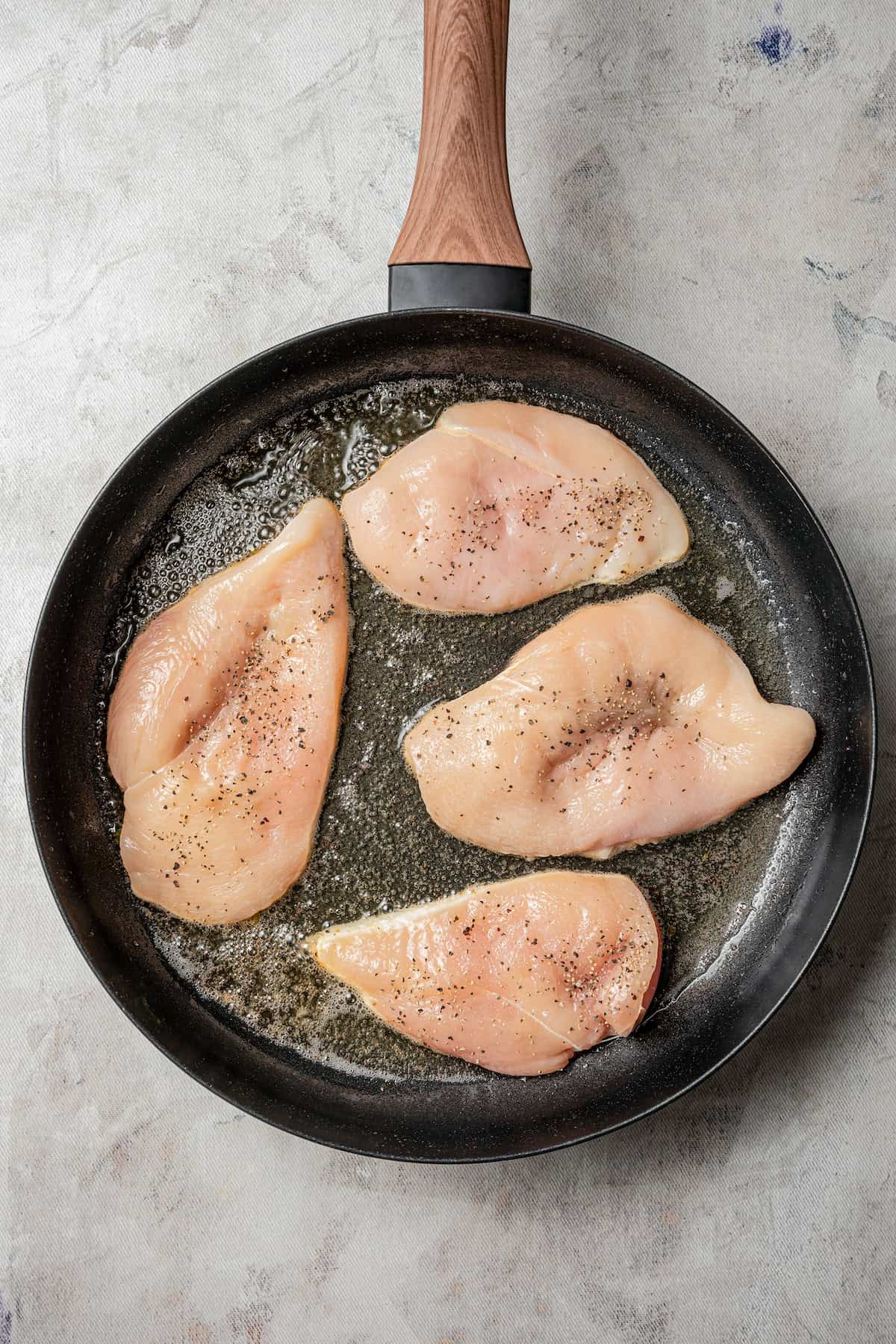 Chicken breasts searing in a skillet.