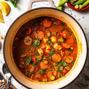 A pot of gumbo surrounded by small bowls of ingredients.