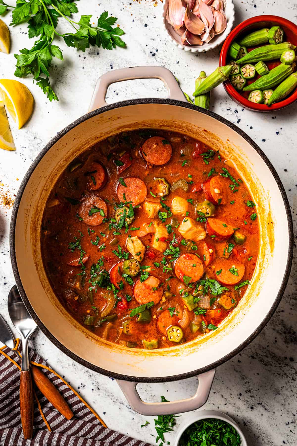 A pot of gumbo surrounded by small bowls of ingredients.