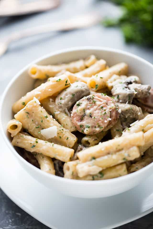 Creamy ziti with sausages and mushrooms served in a white bowl.