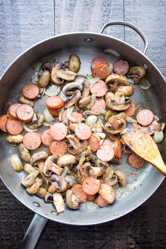 Sauteeing sliced andouille sausages and sliced mushrooms in a large skillet.