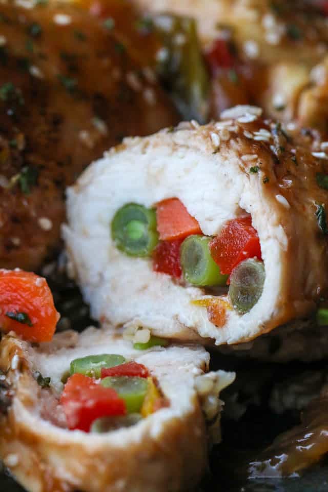 These chicken roll-ups are thinly sliced chicken breasts stuffed with colorful vegetables and cooked in a sweet-savory honey garlic marinade. Close up of a cooked chicken roll up cut in half to reveal the vegetables in the middle.