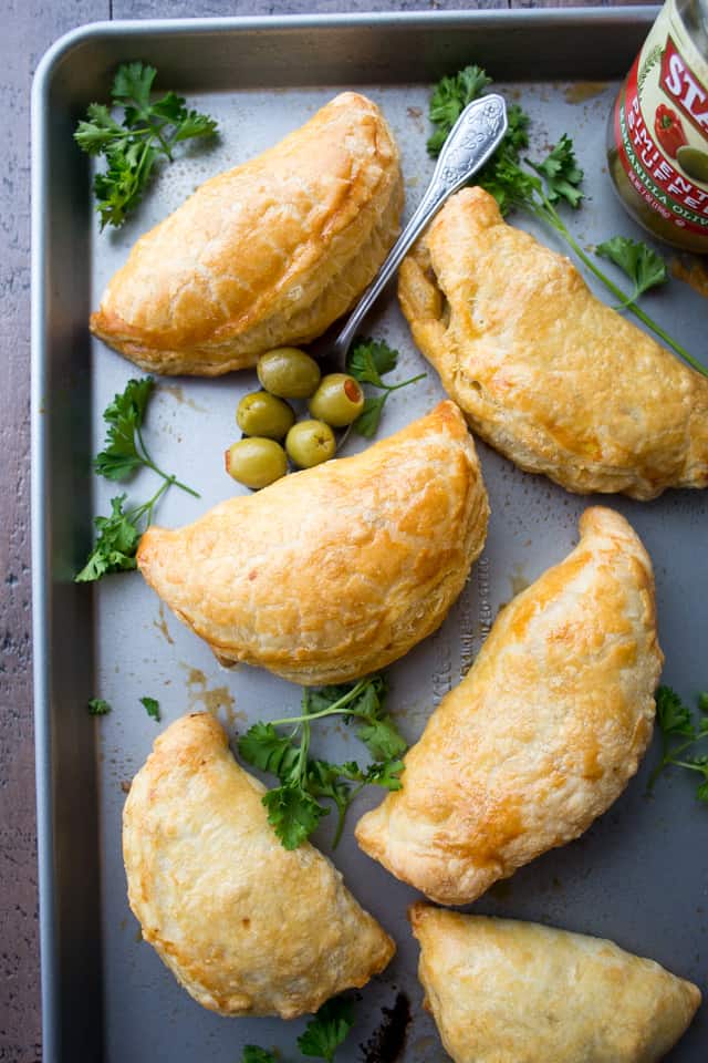 Overhead view of beef empanadas on a tray next to a spoonful of olives.