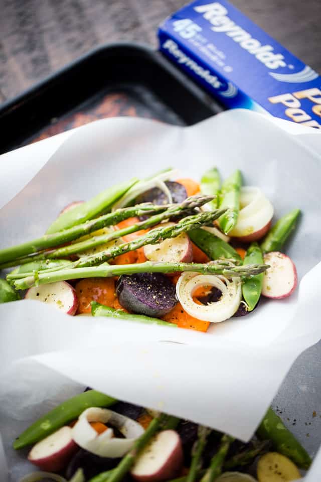 Asparagus, snap peas, carrots, and potatoes are tossed in olive oil and garlic, then roasted in parchment paper packets until tender. Halved small potatoes, sliced fennel, and asparagus stalks are arranged inside a parchment packet.