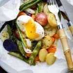 Asparagus, halved potatoes, carrots, snap peas, and a halved boiled egg are all arranged on a sheet of parchment.