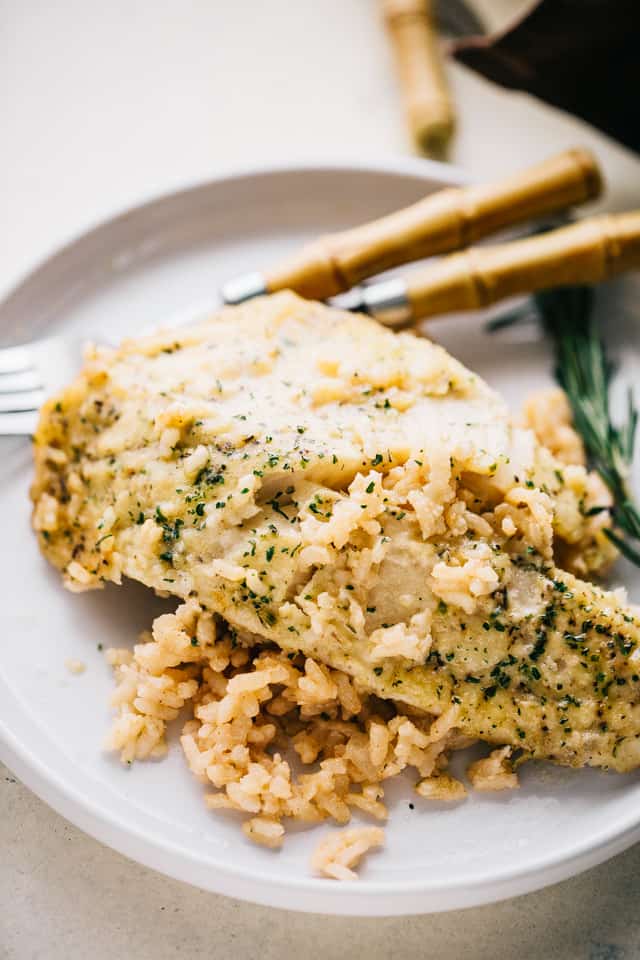 Flaky lemon garlic tilapia is nestled over a bed of creamy risotto rice and baked in one pan for a flavorful, easy weeknight fish dinner! A lemon garlic tilapia filet served over a bed of risotto on a plate.