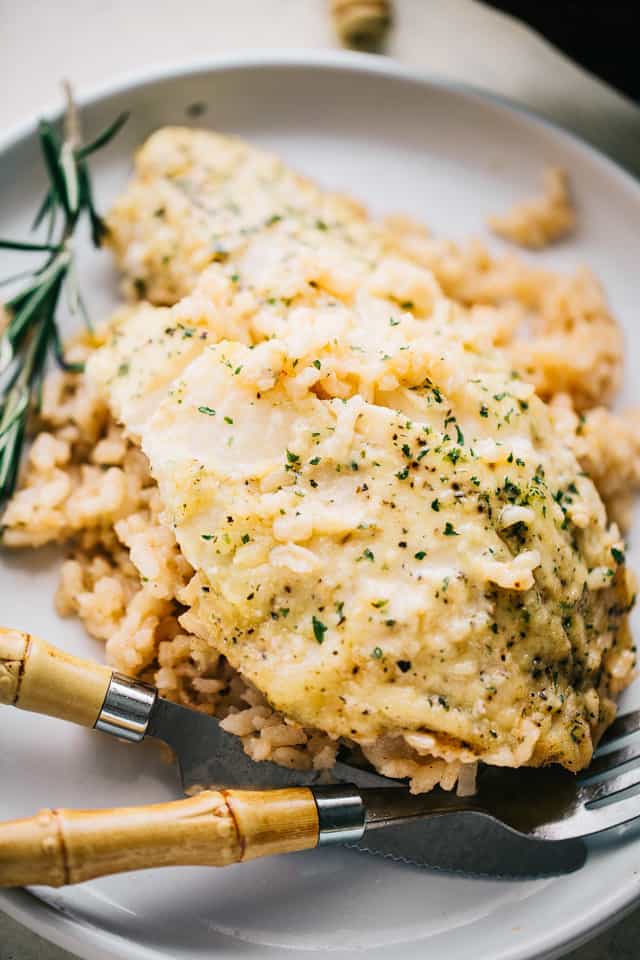Flaky lemon garlic tilapia is nestled over a bed of creamy risotto rice and baked in one pan for a flavorful, easy weeknight fish dinner! A lemon garlic tilapia filet served over a bed of risotto on a plate.