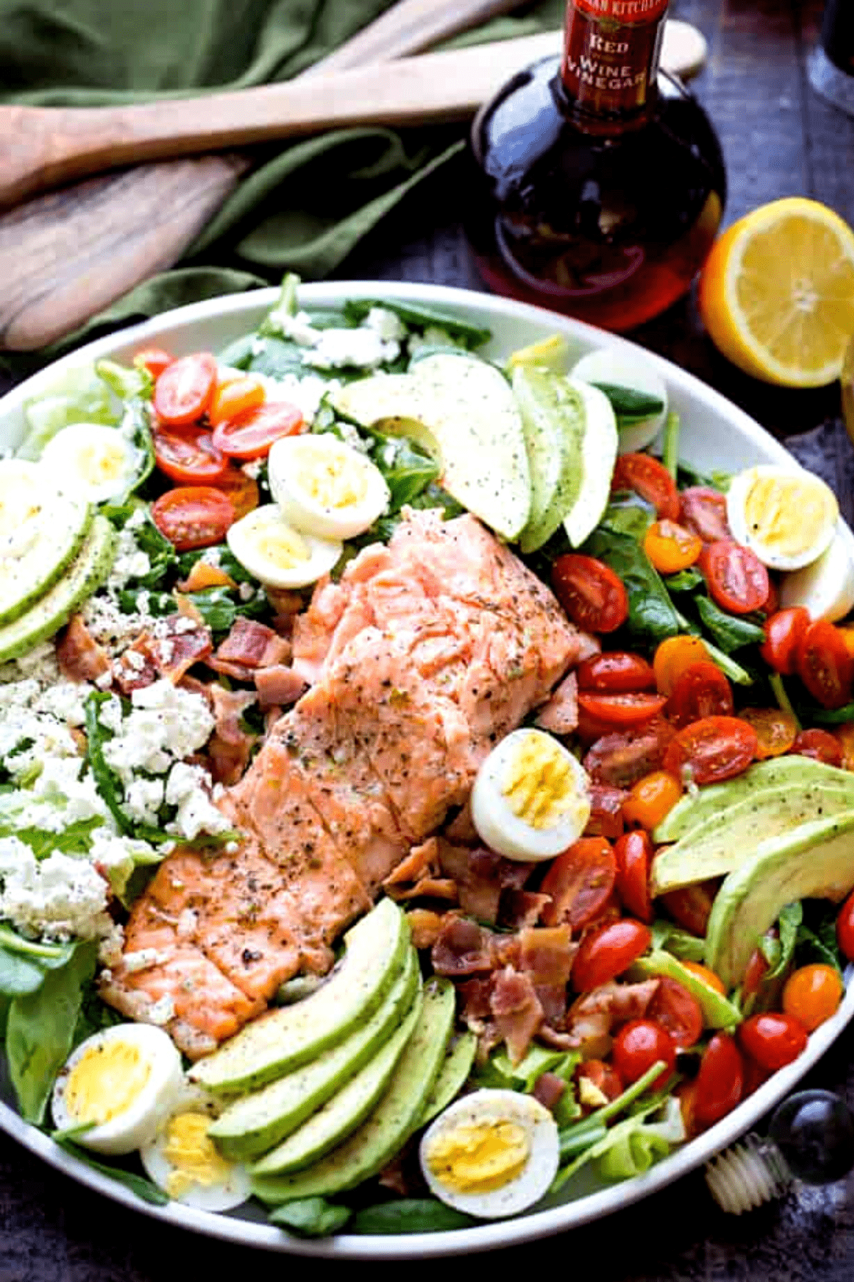 overhead shot of Salmon Cobb Salad with Spinach and Feta - Tender spinach and romaine lettuce topped with delicious oven-baked salmon, tomatoes, eggs, bacon, avocados and feta, all tossed together with a tangy lemon-mustard dressing.